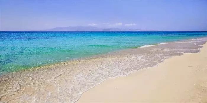 Una spiaggia sabbiosa con acqua azzurra e le montagne imperiali sullo sfondo.