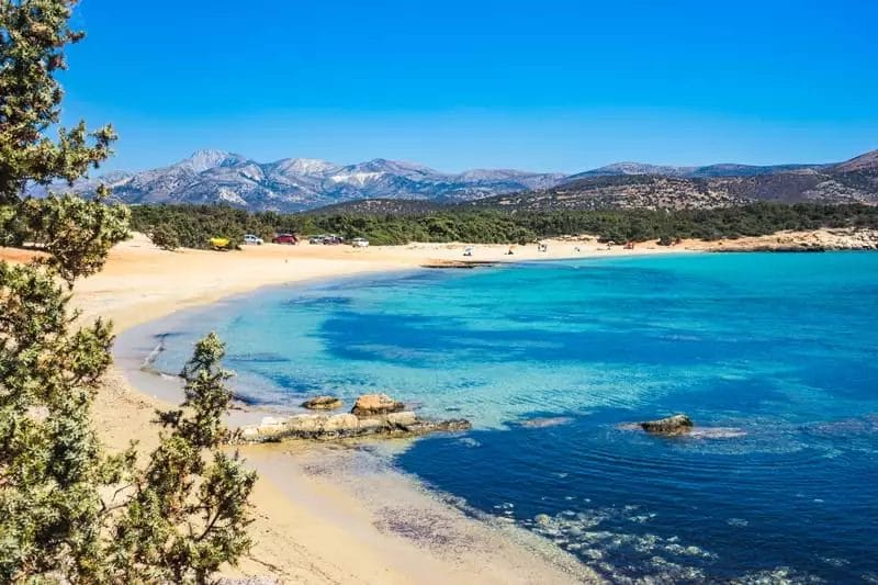 Una spiaggia tranquilla con acque cristalline, sabbia dorata, barche ancorate e uno sfondo di montagne e vegetazione nel resort VERACLUB NAXOS.