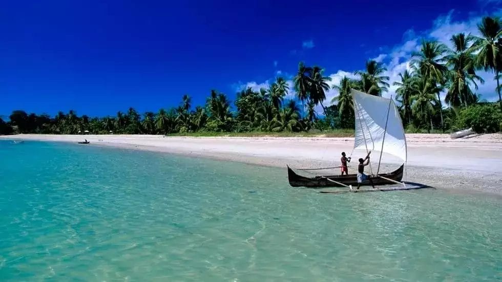 Barca a vela tradizionale vicino all'Andilana Beach Resort con acque cristalline e palme.