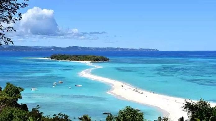 Una vista panoramica di Andilana Beach, una spiaggia tropicale con acque cristalline, barche e un'area boschiva circostante.