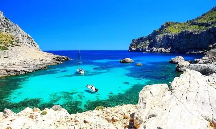 Una barca è ormeggiata in acqua vicino alle scogliere rocciose del beach club Font de Sa Cala.