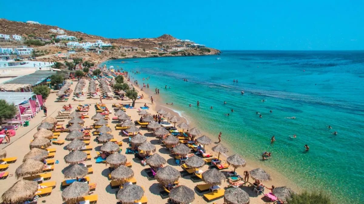 Una scena soleggiata al Paradise Beach Resort con file di ombrelloni e lettini dal tetto di paglia, con persone che si godono il mare cristallino.