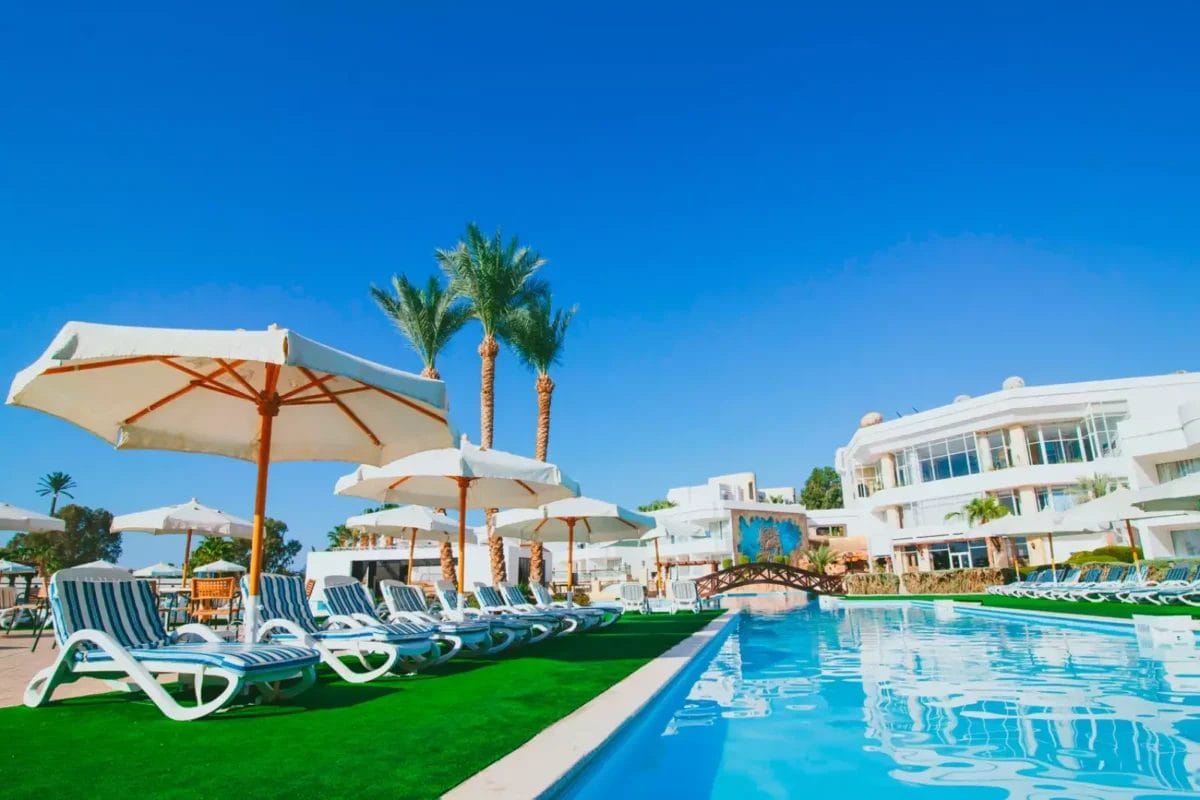 Lussuoso rifugio a bordo piscina del Queen Sharm Resort con lettini e ombrelloni che offre un luogo perfetto per rilassarsi sotto il cielo azzurro.