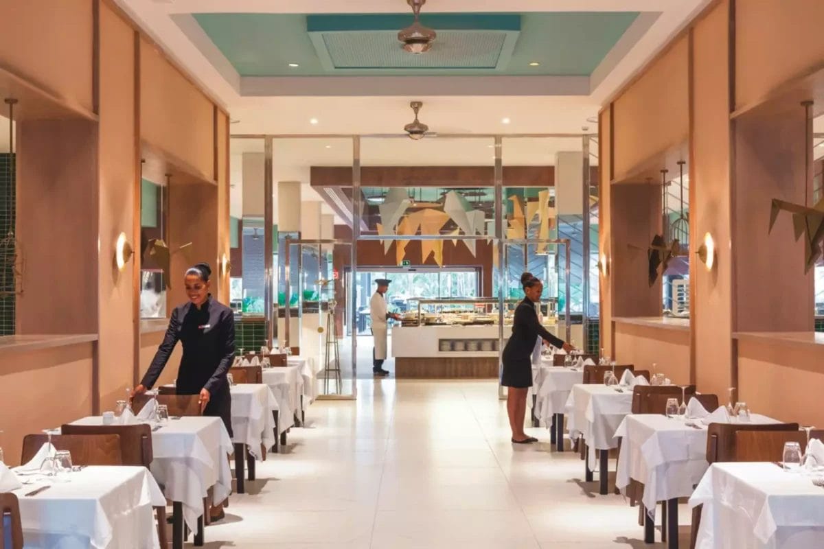 Interno di un elegante ristorante RIU Cabo Verde con personale e tavoli apparecchiati.