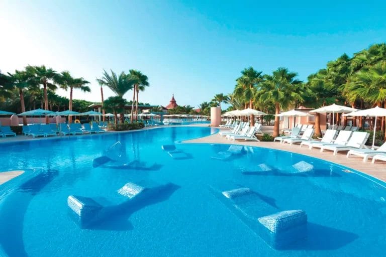 Una piscina del RIU Resort a Capo Verde, con lettini in acqua e palme sotto un cielo azzurro e limpido.