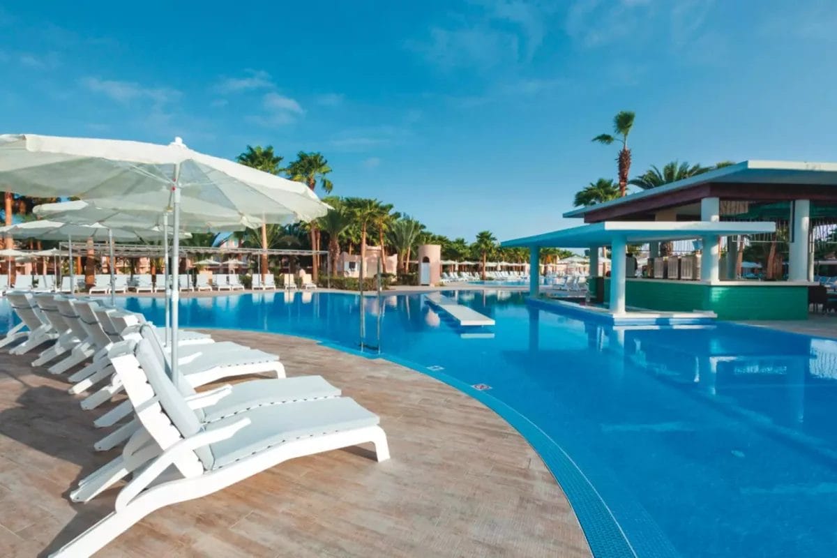 La tranquilla piscina del resort RIU Cabo Verde, circondata da lettini bianchi e ombreggiata da ombrelloni in una giornata di sole.