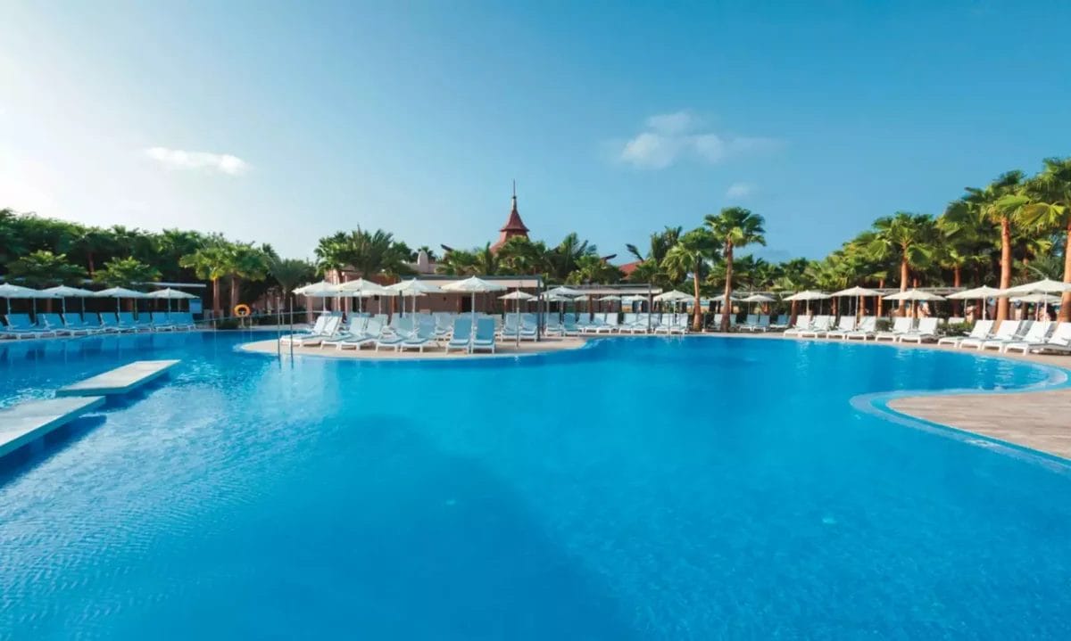 Una tranquilla piscina del resort RIU Cabo Verde, fiancheggiata da lettini e ombrelloni bianchi, sotto un cielo azzurro e limpido.