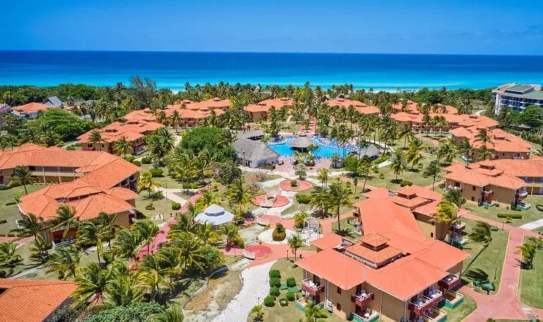 Veduta aerea del resort ROC Arenas Doradas a Varadero, Cuba, con tetti di tegole rosse, circondato da una vegetazione lussureggiante e affacciato su un mare cristallino.