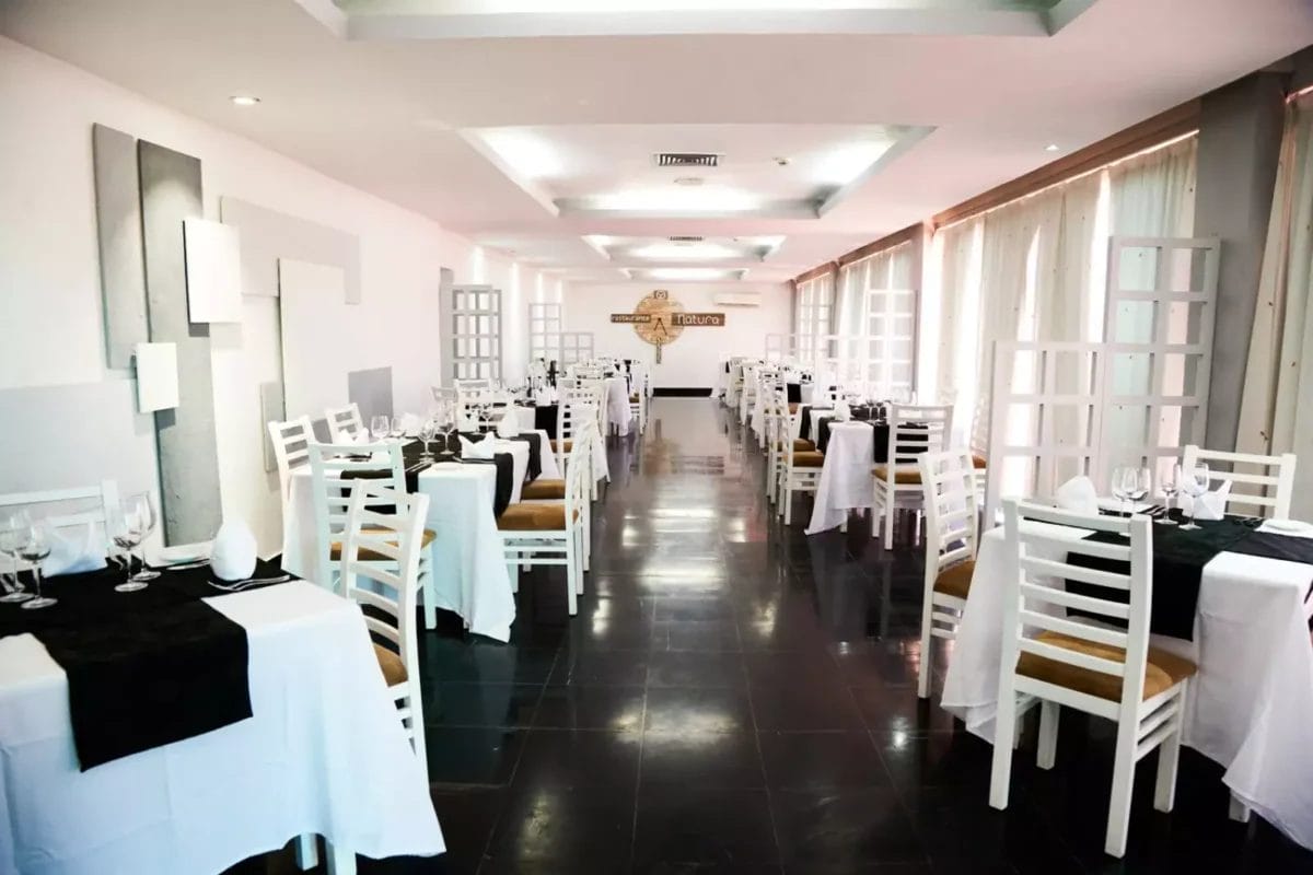 Un interno moderno e ben organizzato dell'hotel ristorante ROC ARENAS DORADAS a Varadero, con sedie bianche e nere, tavoli apparecchiati con tovaglie bianche e illuminazione ambientale.