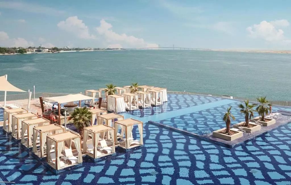 Una piscina con sedie a sdraio e ombrelloni sulla spiaggia del Royal M Hotel, Abu Dhabi.