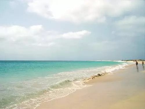 Giornata di sole in spiaggia al RIU Cabo Verde con calme acque turchesi e poche persone che camminano sulla riva sabbiosa.