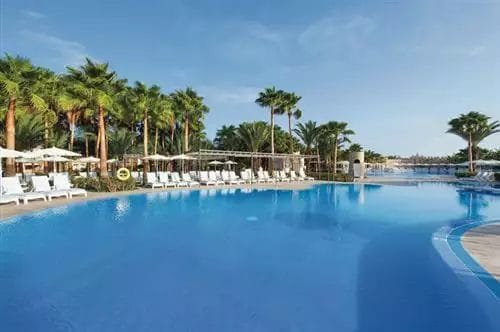 Una tranquilla piscina del RIU Resort a Capo Verde, circondata da palme e lettini sotto un cielo azzurro e limpido.