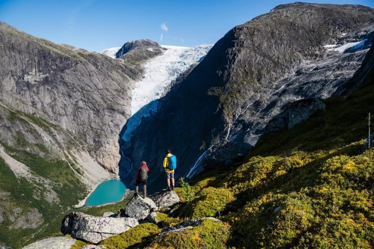 Due escursionisti affacciati su un paesaggio glaciale con un lago turchese nei Fiordi Norvegesi.