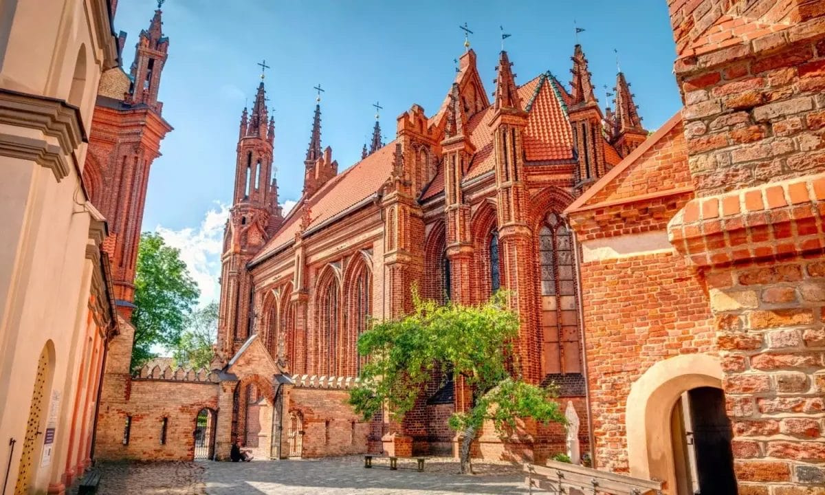 Una vista soleggiata di una chiesa gotica in mattoni con intricati dettagli architettonici, parte di una Tour Capitali Baltiche.