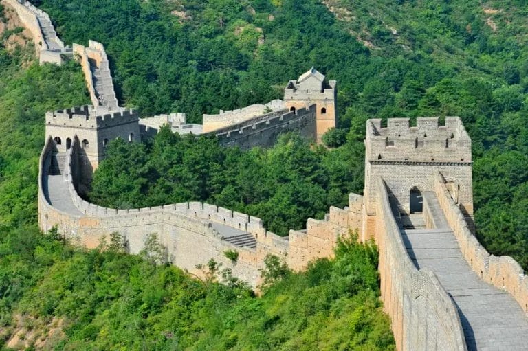 Un segmento della Grande Muraglia Cinese che si snoda attraverso un paesaggio lussureggiante e collinare, incarnando l'essenza di un "viaggio Cina.