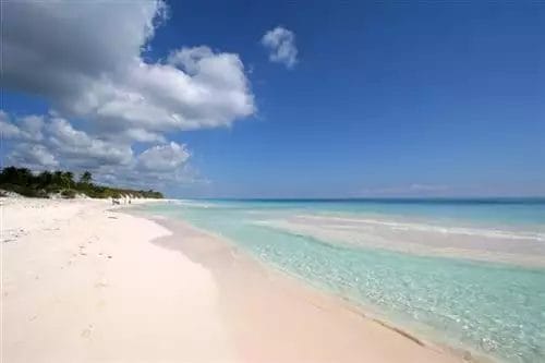 Una tranquilla spiaggia tropicale a Tulum con cielo azzurro, sabbia bianca e acqua turchese.