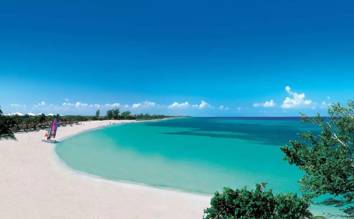 Una spiaggia tropicale incontaminata a Varadero, Cuba, con acque turchesi, sabbia bianca e un'unica barca a vela colorata ancorata vicino alla riva.