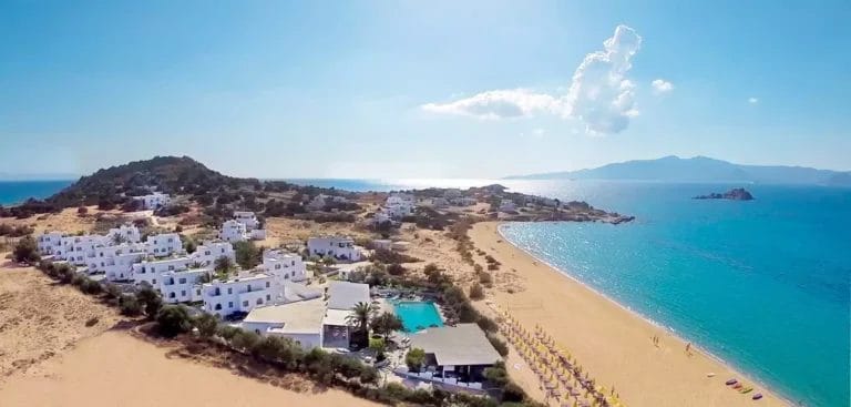 Veduta aerea di un villaggio costiero con edifici bianchi, una spiaggia sabbiosa e acque cristalline a VERACLUB NAXOS.