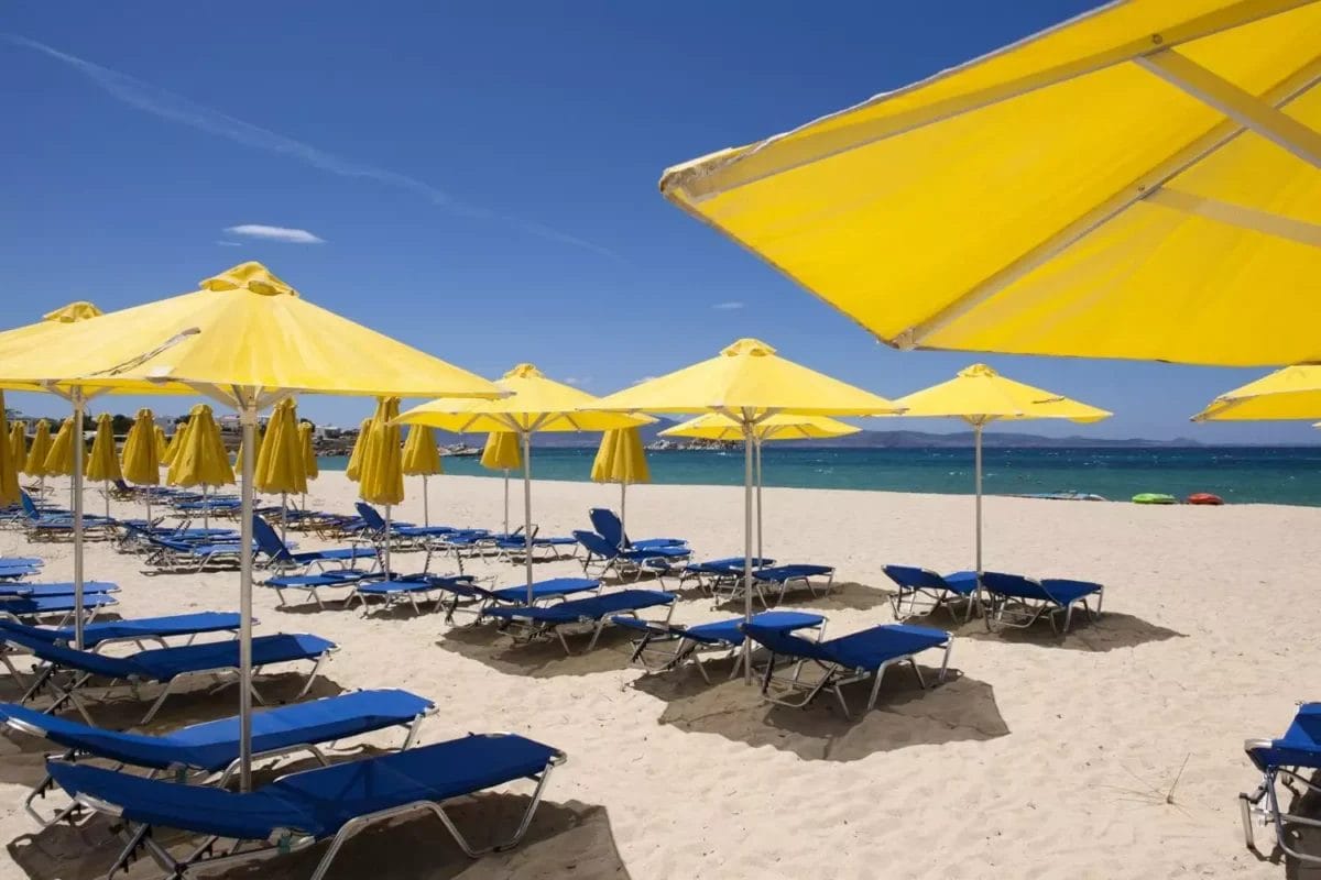 Fila di sedie a sdraio blu e ombrelloni gialli su una spiaggia sabbiosa a VERACLUB NAXOS.