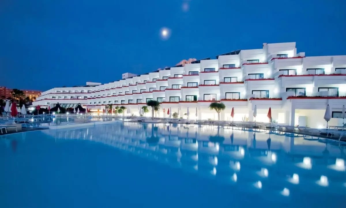 Serenità crepuscolare in un moderno resort VeraClub Gala con una piscina tranquilla che riflette la frizzante architettura bianca sotto un cielo illuminato dalla luna.