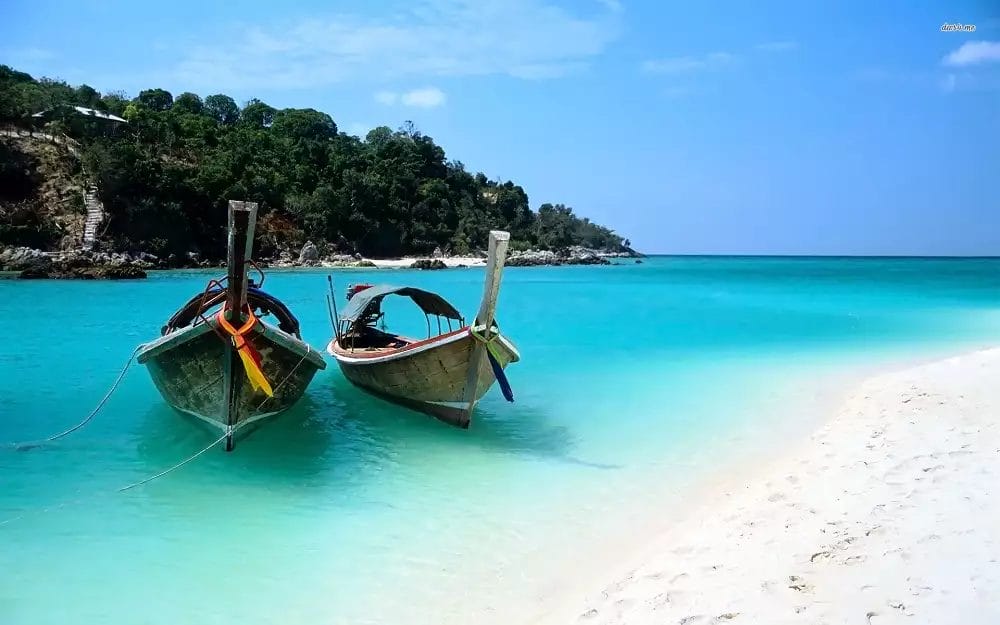 Due barche a coda lunga ormeggiate su una spiaggia di sabbia bianca con acque turchesi limpide sotto il cielo blu di Sun Bay.