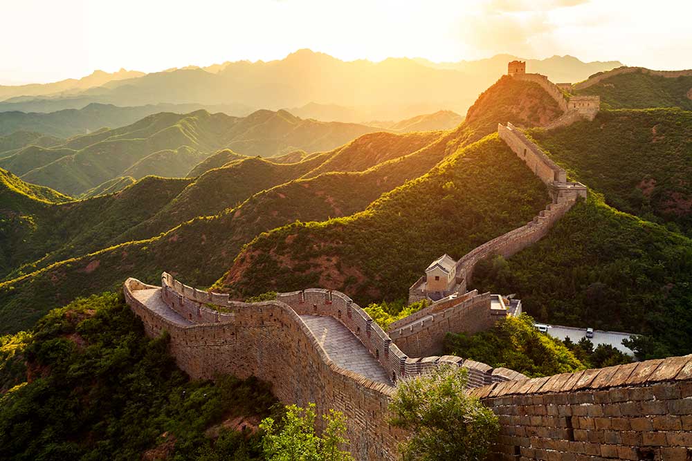 La Grande Muraglia della Cina si snoda attraverso lussureggianti montagne al tramonto.