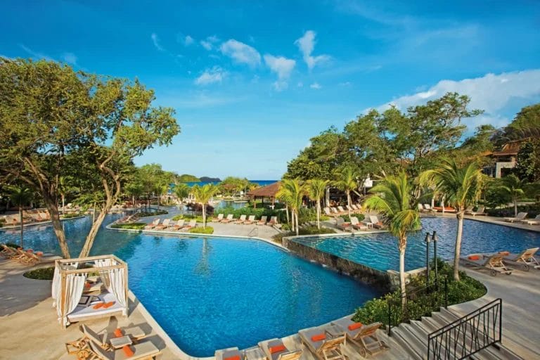 Piscina tropicale con sedie a sdraio e vegetazione lussureggiante sotto un cielo blu al Dreams Las Mareas Luxury Resort in Costa Rica.