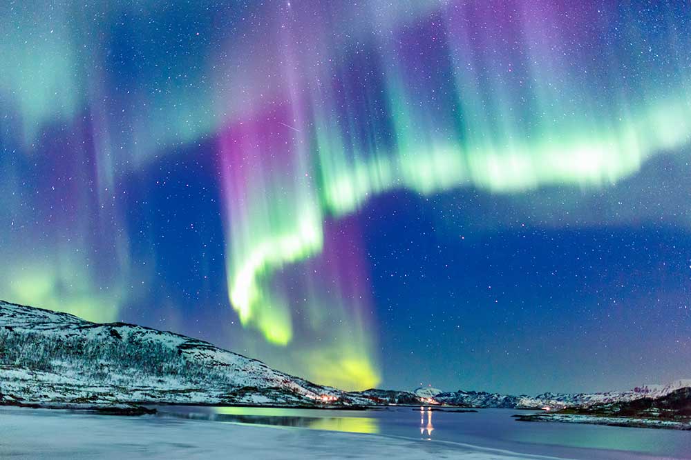 Uno spettacolo vibrante dell'aurora boreale su un paesaggio innevato nel Nord Europa con un lago parzialmente ghiacciato.