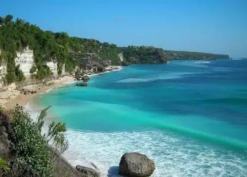 La pittoresca vista costiera di Nusa Dua offre acque turchesi e cristalline, scogliere rocciose e una vegetazione lussureggiante sotto un cielo azzurro, il tutto arricchito dalla serenità di una spa nelle vicinanze.