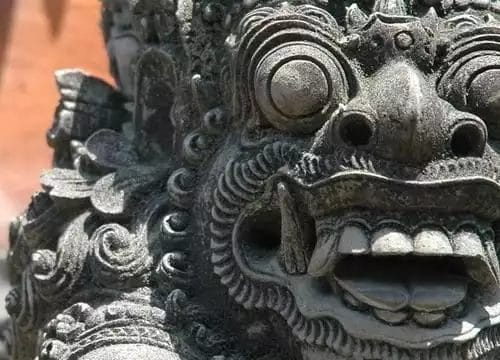 Primo piano di una scultura in pietra dettagliata in un hotel sulla spiaggia di Nusa Dua, raffigurante una creatura mitica con grandi occhi e bocca aperta, che si sposa perfettamente con la tranquilla atmosfera della spa.