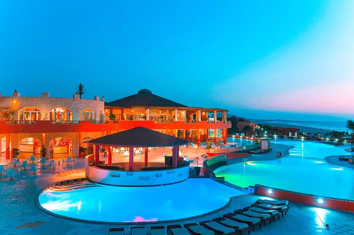 All'Occidental Boa Vista, una vivace area piscina si anima al tramonto. Piscine illuminate e un bar circolare completano l'edificio rosso con balconi, il tutto sullo sfondo di un cielo serale limpido e colorato: una fuga perfetta vicino alla spiaggia di Boa Vista.