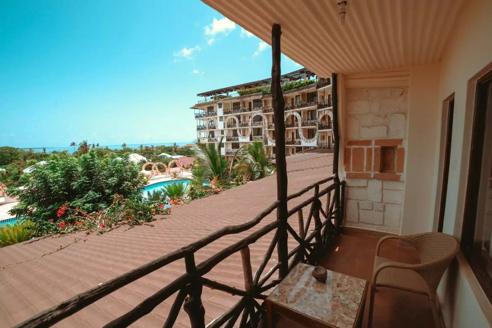 Il balcone offre una vista mozzafiato sul Palumbo Waves Resort, che mette in mostra i suoi eleganti edifici, la piscina scintillante, gli alberi rigogliosi e l'oceano in lontananza sotto un cielo azzurro e limpido. Un grazioso tavolo e sedie vi invitano a sedervi e a godervi il tranquillo scenario.