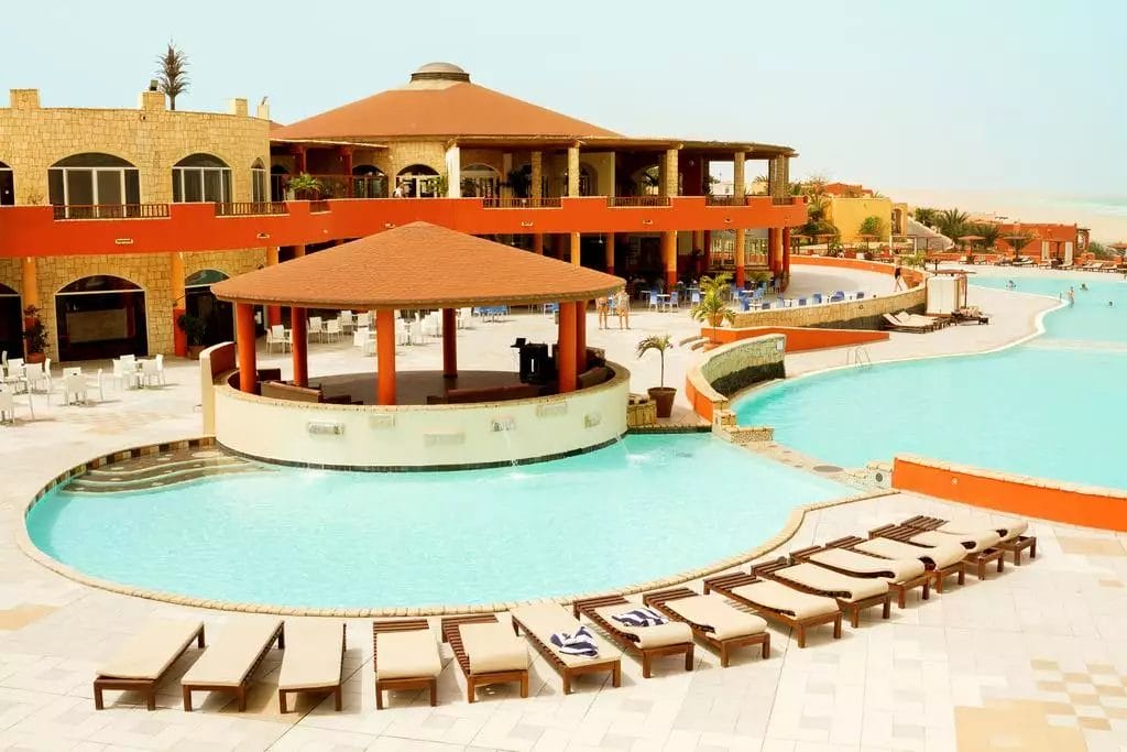 L'area della piscina esterna dell'Occidental Boa Vista è dotata di lettini prendisole e di un padiglione centrale, il tutto in contrasto con la facciata rossa e gialla del grande edificio circostante. A due passi dalla spiaggia di Boa Vista, è un luogo idilliaco per rilassarsi.
