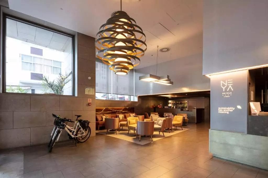 La moderna hall del Neya Lisboa Hotel vanta un'accogliente area salotto, grandi lampade a sospensione e due biciclette vicino all'ingresso. Le sue pareti minimaliste sono adornate da ampie finestre, creando uno spazio invitante che cattura il fascino vibrante di Lisbona.