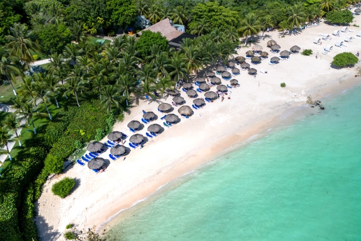 Vista aerea della spiaggia tropicale del BRAVO DECAMERON BARU con ombrelloni di paglia, sedie a sdraio, palme e acqua turchese.