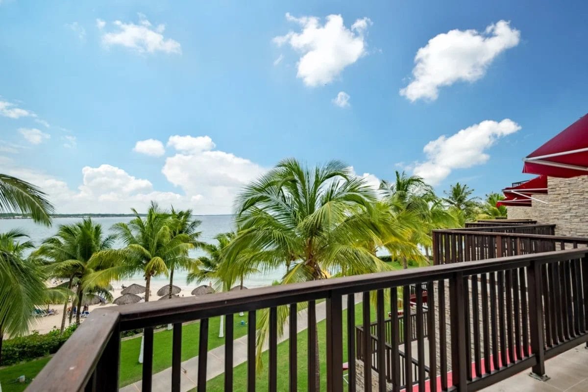 Godetevi una vista mozzafiato dal vostro balcone del BRAVO DECAMERON BARU, con vista sulle palme, sulla spiaggia sabbiosa e sull'oceano scintillante sotto un cielo azzurro brillante con nuvole.
