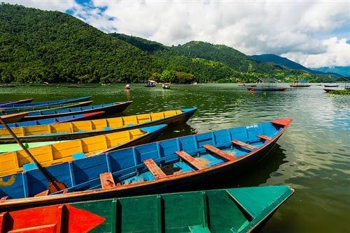 Barche di legno colorate su un lago calmo con verdi colline e cielo nuvoloso sullo sfondo.