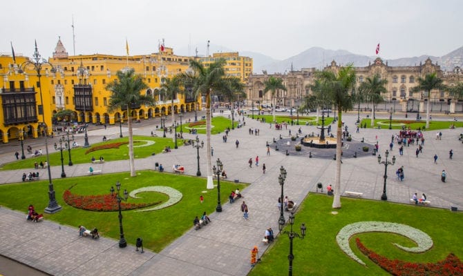 Una piazza cittadina esclusiva in Perù, con edifici coloniali gialli, palme e persone che passeggiano lungo sentieri che attraversano prati verdi: una destinazione invitante da esplorare nel 2025.