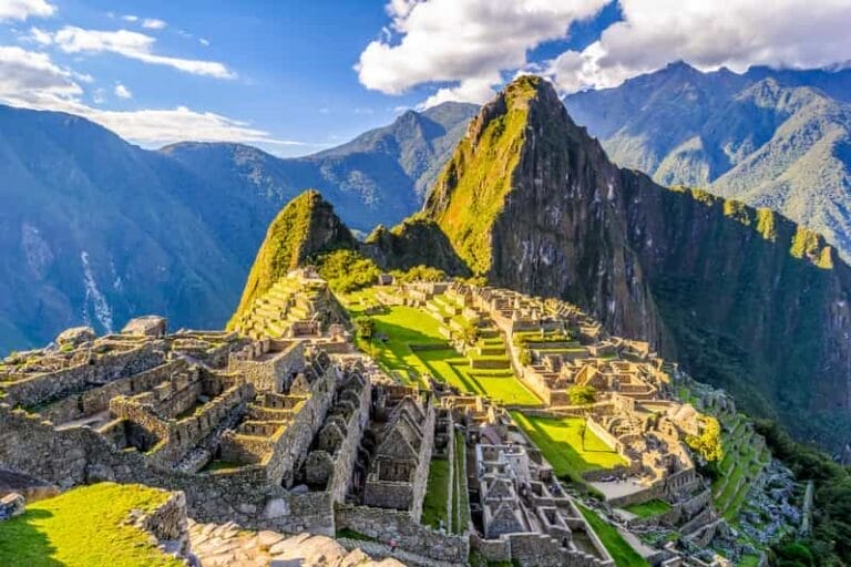 Scopri le antiche rovine in pietra di Machu Picchu in Perù, immerse tra lussureggianti montagne verdi sotto un cielo luminoso: perfette per un indimenticabile viaggio esclusivo nel 2025.