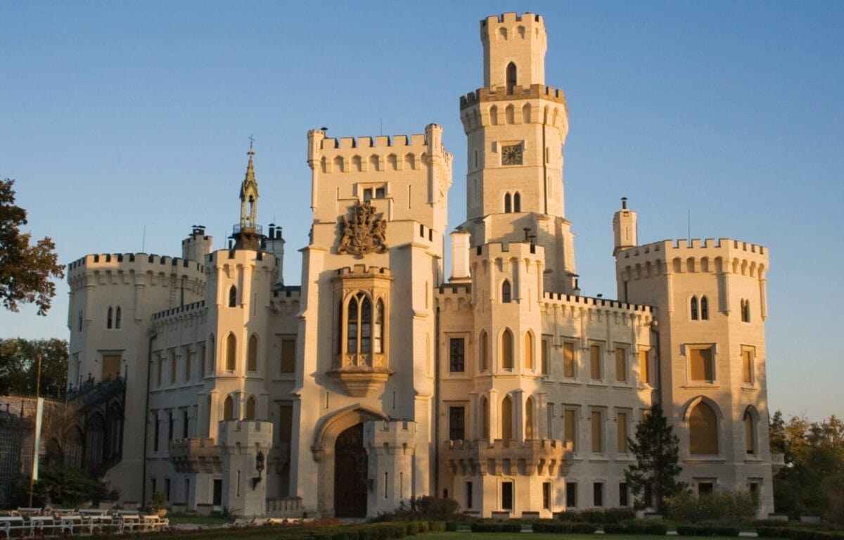 Un grande castello bianco con torri e mura merlate, immerso nella calda luce del sole contro un cielo limpido: una vista iconica per qualsiasi TOUR dei CASTELLI DELLA BOEMIA vicino a PRAGA.