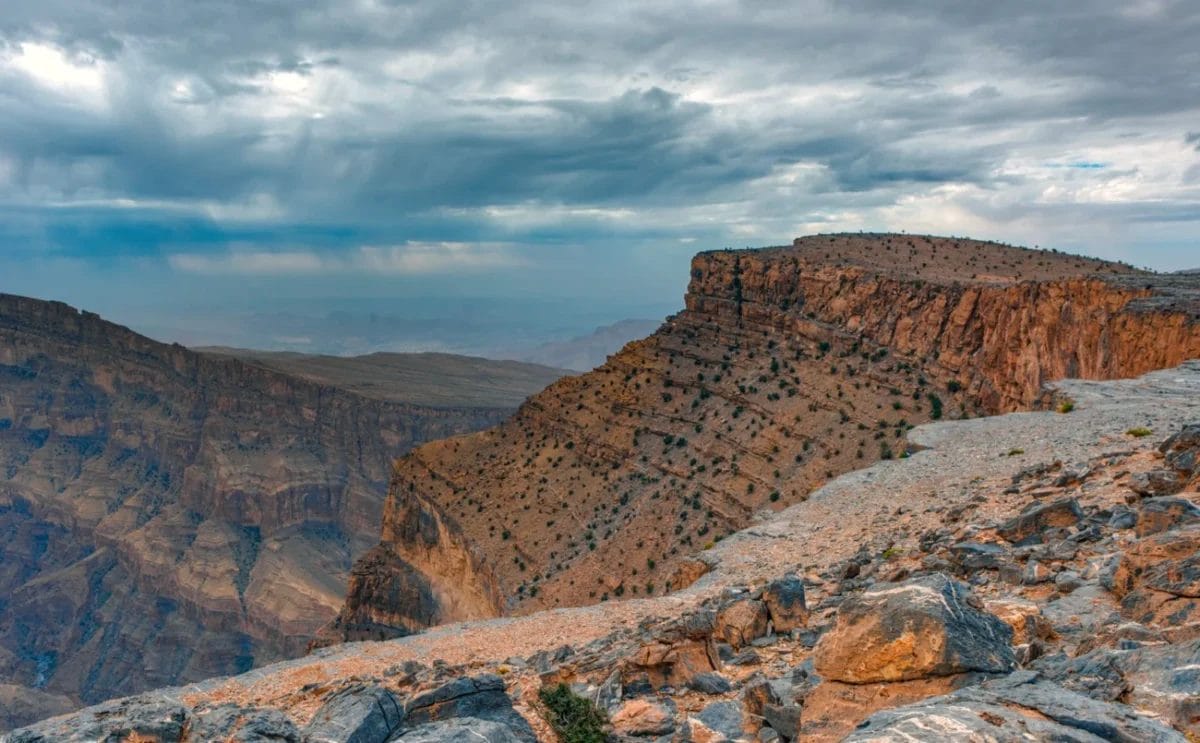 Drammatiche scogliere rocciose del canyon sotto un cielo nuvoloso con montagne lontane all'orizzonte.