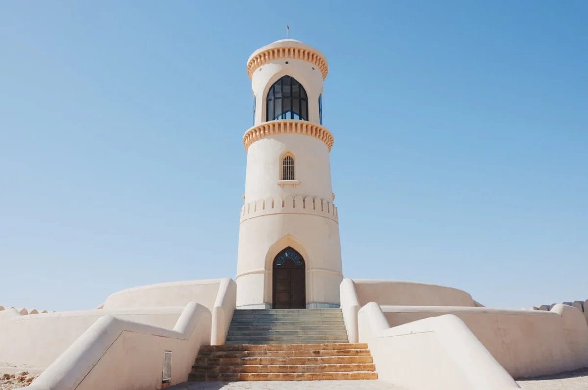 Faro bianco con finestre e scale ad arco, sullo sfondo di un cielo azzurro e limpido.