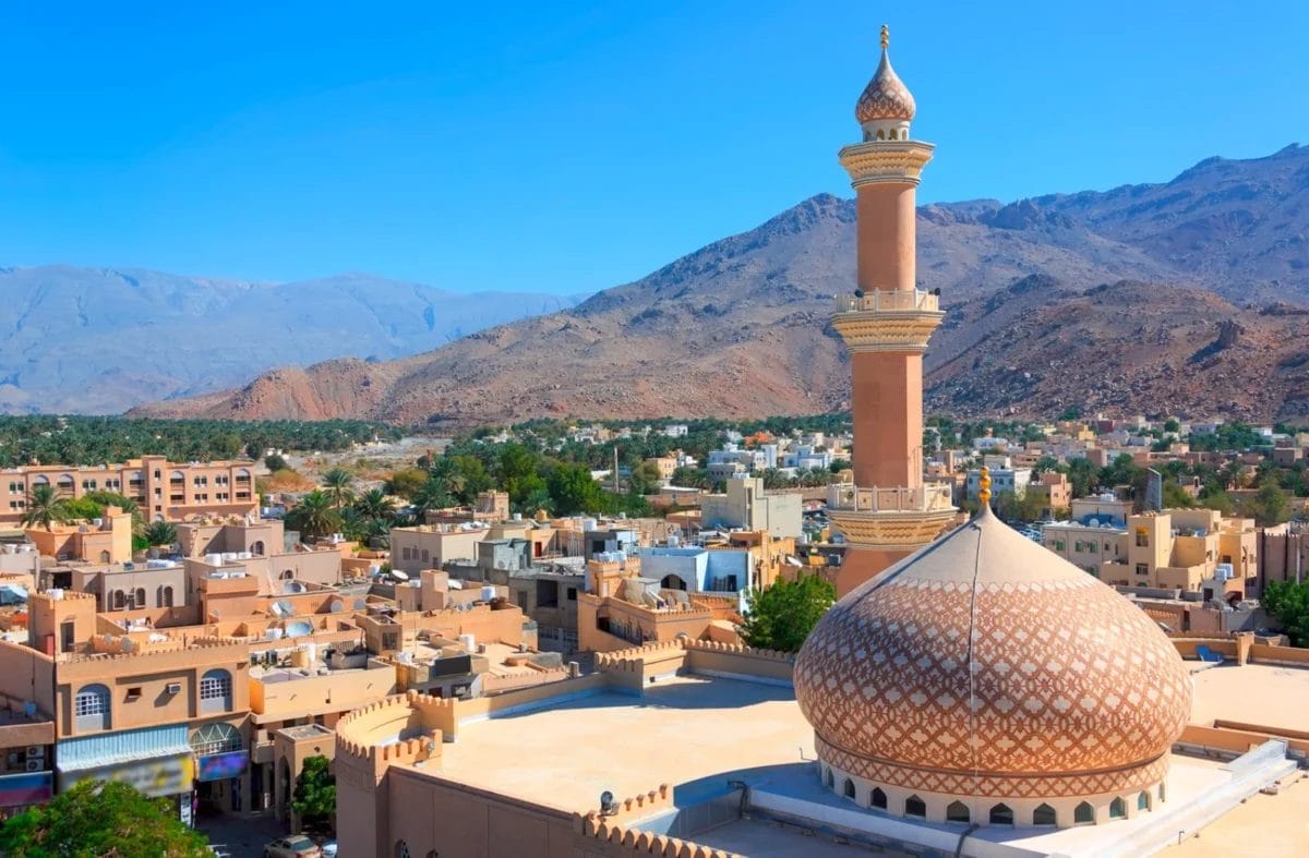 Una moschea con cupola a motivi e alto minareto in una città del deserto con le montagne sullo sfondo.