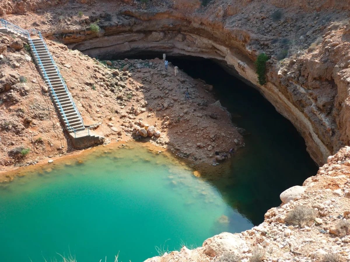 Una dolina di acqua turchese circondata da un terreno roccioso con scale che scendono fino al bordo.