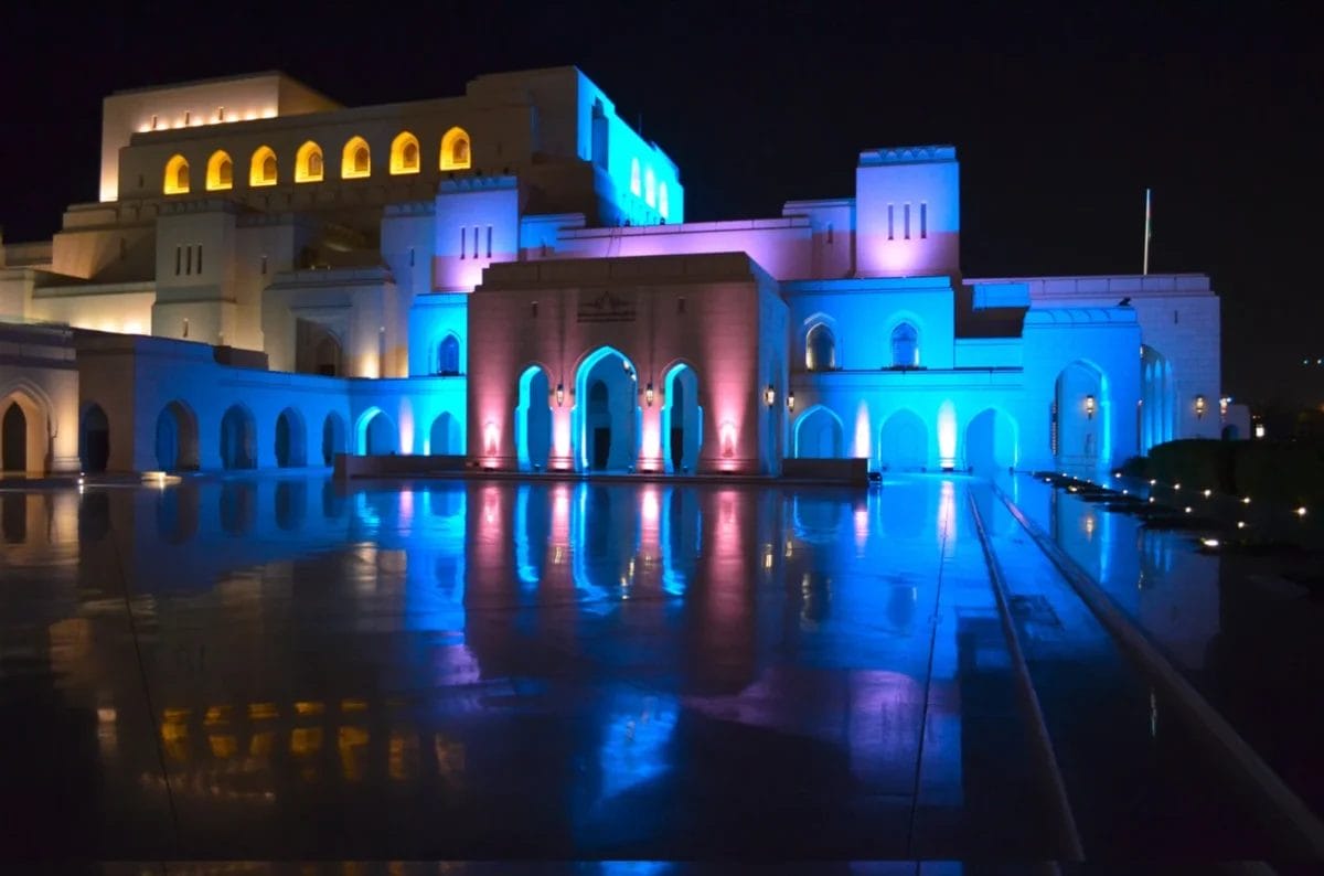 Un grande edificio illuminato con luci blu e gialle, che di notte si riflette su una superficie lucida.