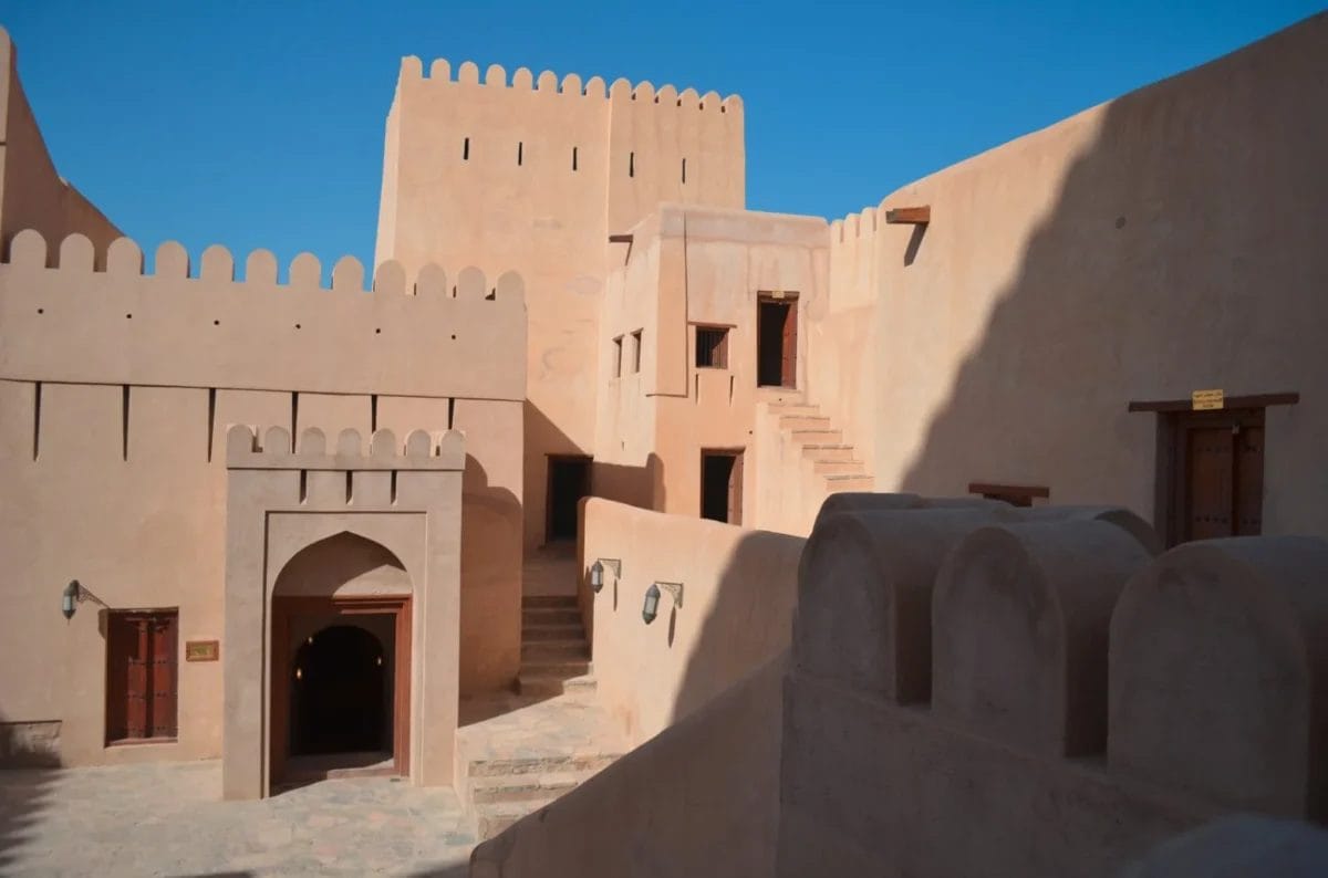 Un forte del deserto illuminato dal sole, con pareti beige, ingressi ad arco e un cielo azzurro e limpido.