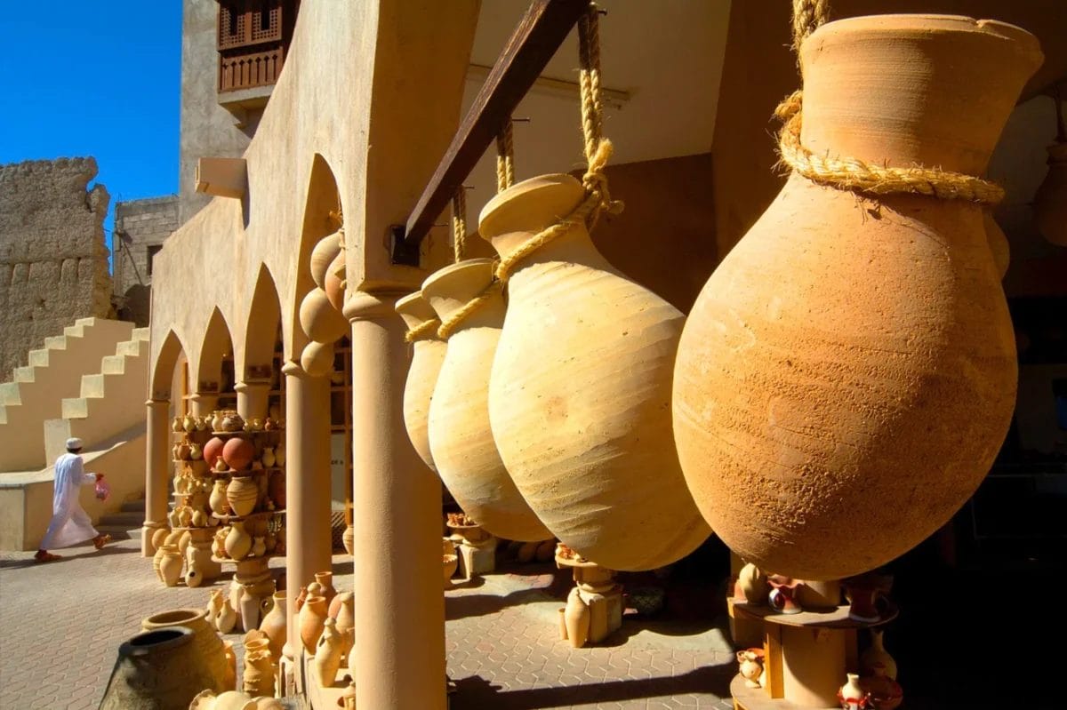 Grandi vasi di argilla appesi all'esterno di un tradizionale mercato mediorientale con archi e ceramiche in esposizione.