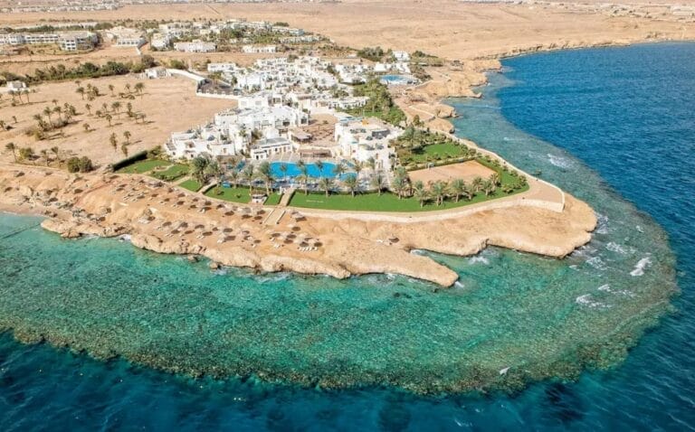 Vista aerea del Veraclub Sharm, un resort costiero a Sharm el Sheikh con edifici bianchi, piscine, palme e acque cristalline.
