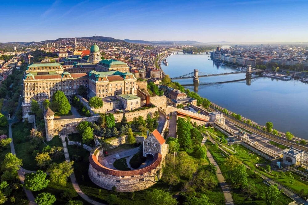 Vista aerea del Castello di Buda a Budapest, in Ungheria, con il fiume Danubio e il Ponte delle Catene nelle vicinanze. Alberi e giardini verdeggianti circondano lo storico castello, una tappa obbligata di qualsiasi tour in pullman da Praga a Budapest.