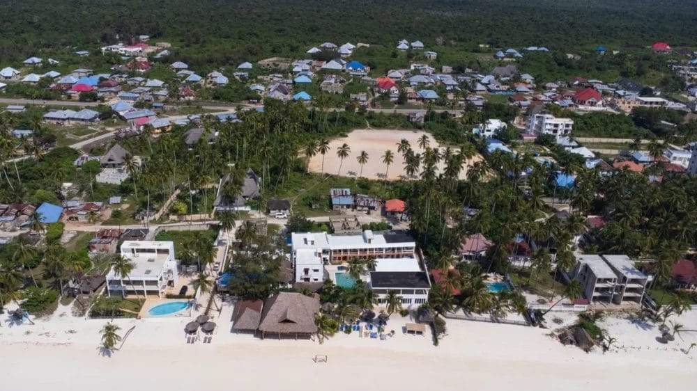 Veduta aerea di Marlin Beach, con spiagge di sabbia bianca, edifici sulla spiaggia, palme e case immerse nel verde. Un'ampia area aperta si trova al centro della città, vicino al BLU MARLIN BEACH RESORT.